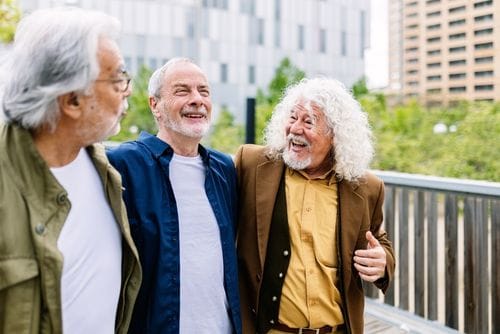 Drei Männer mit grauen Haaren lachen und gehen durch die Stadt 500x334px